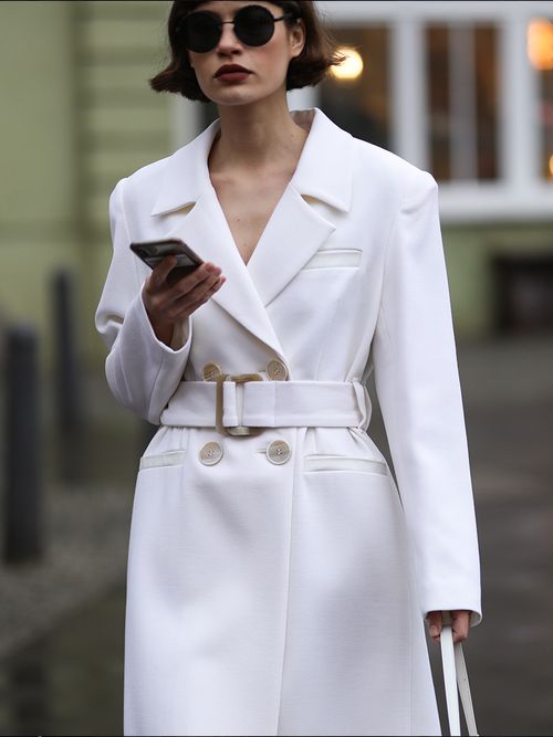 Streetstyle mit weißen Mantel und schwarzer runder Sonnenbrille.