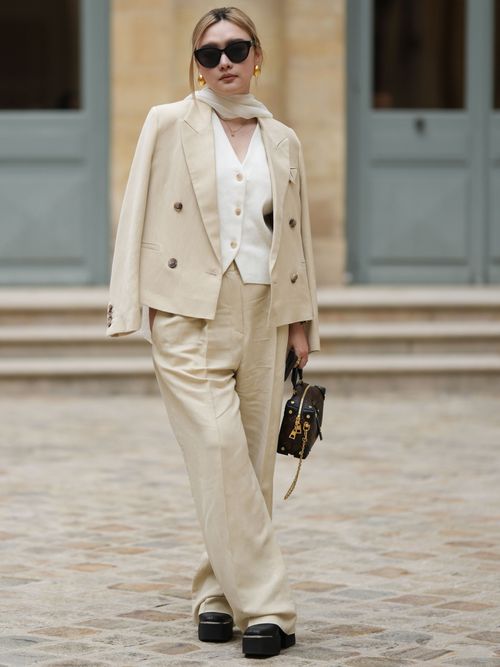 Street Style Look in Paris, wo ein Gast einen beigen Leinen Anzug mit weißer Anzugweste und Boots trägt.