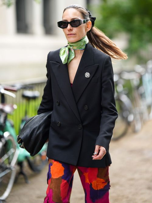 Street Style Look von der Copenhagen Fashion Week, wo ein Gast einen schwarzen Blazer mit einer Blumenprinz-Hose und Halstuch trägt.