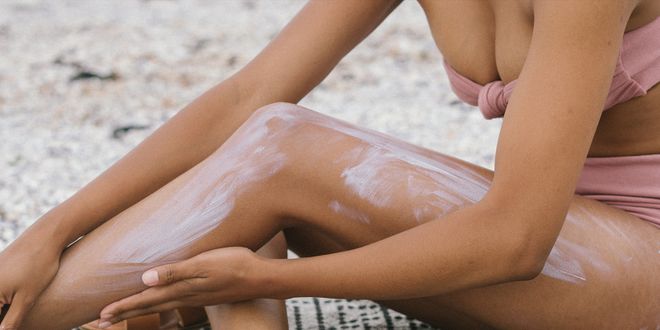 Frau in einem altrosa Bikini, die sich am Strand eincremt.