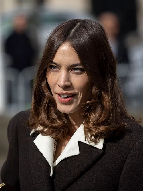 Alexa Chung mit leicht gewellten Haaren zu einem schwarzen Mantel und einer weißen Bluse.