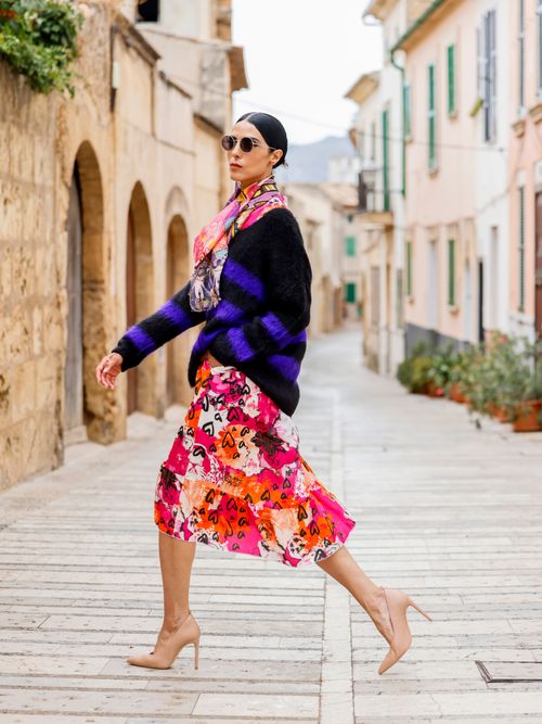 Model Zoe Helali trägt einen gestreiften Wollpulli, floralen Blumenrock, Halstuch und nudefarbene Pumps auf Mallorca.