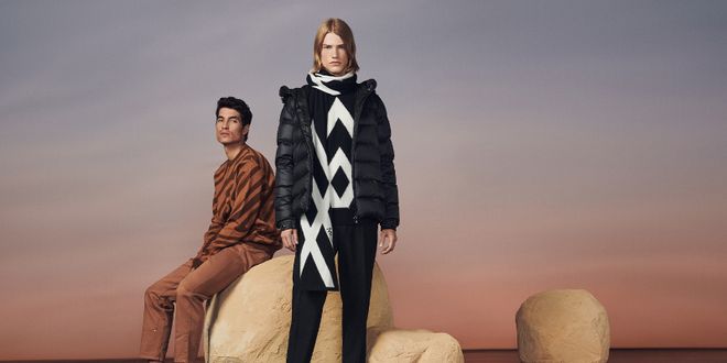 Zwei Männer in einer Steinkullisse, einer in einem braunen Outfit und einer in einem schwarzen Outfit.