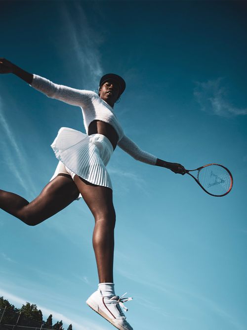 Frau im weißen Tennisoutfit und einem Tennisschläger in der Hand springt in die Luft.