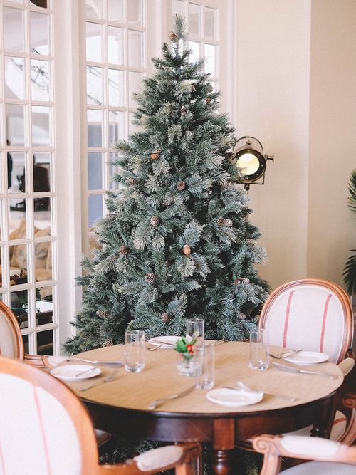 Plastik Christbaum der mit Zapfen geschmückt wurde und hinter einem runden Tisch steht.
