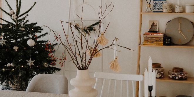 Ein Tisch mit einer weißen Vase vor einem Holzbücherregal und einem Christbaum.