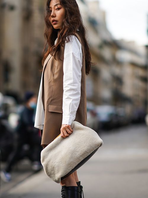 Streetstyle mit einer weißen Bluse und einer braunen Blazerweste zu einer weißen Fell-Clutch.