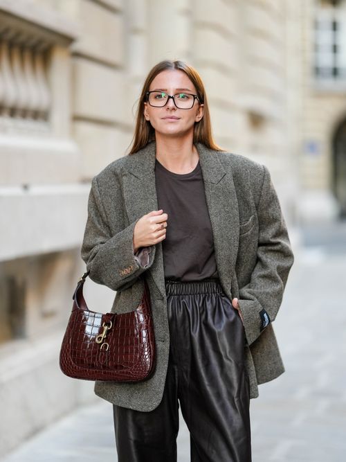 Diane Batoukina trägt einen grauen Wollmantel, braunes T-Shirt, schwarze Lederhose, optische Brille und eine weinrote Gucci-Tasche in Paris.
