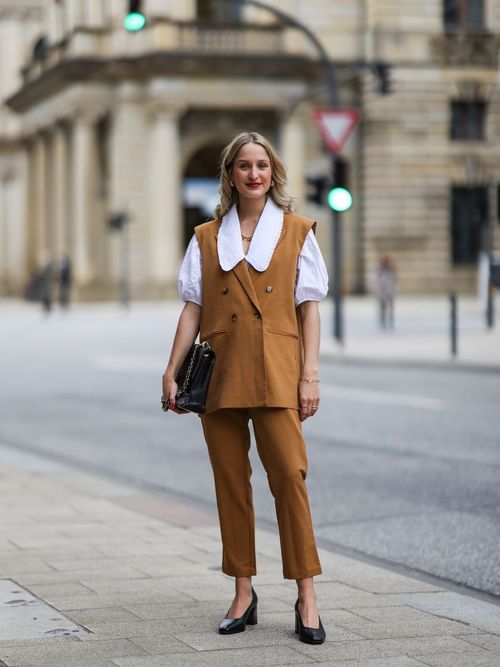 woman wearing brown pants, brown suit vest and white blouse
