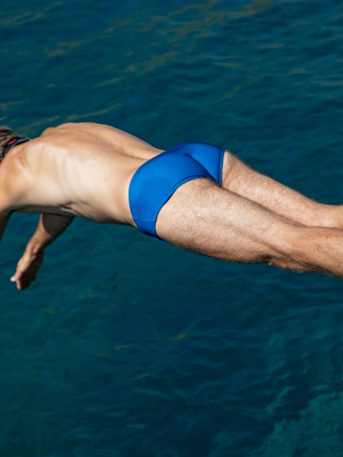 Ein Mann köpfelt mit einer blauen Slip-Badehose ins Wasser.