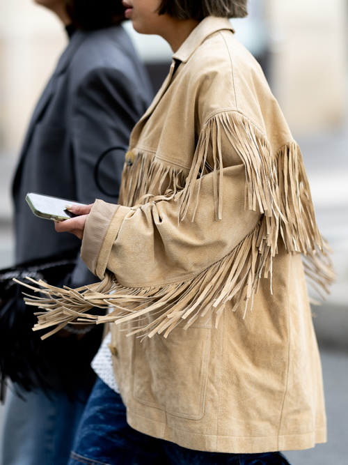 A guest wears a beige suede jacket with fringes outside Stella McCartney show during Womenswear Spring/Summer 2025 as part of Paris Fashion Week on September 30, 2024 in Paris, France.
