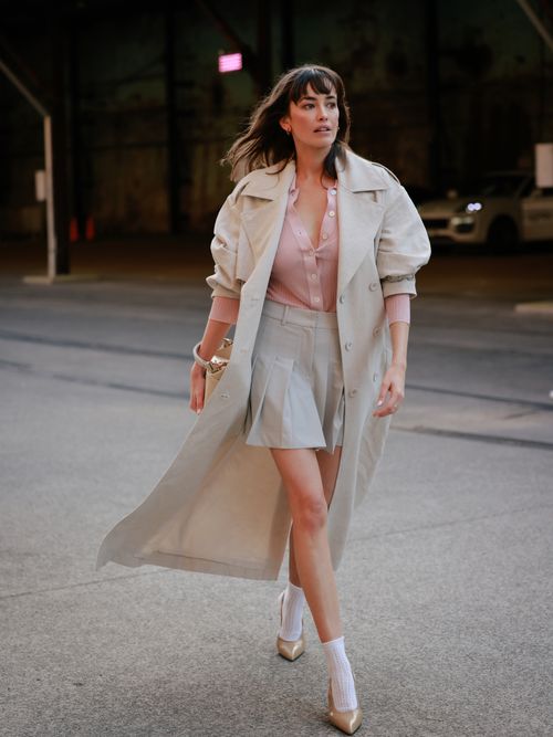 Sarah Stephens trägt einen langen Staubmantel, rosa Bluse, beigen Faltenrock, weiße Socken und nudefarbene Pumps auf der Australian Fashion Week.