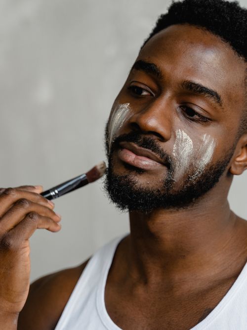 Mann mit Bart trägt sich mit einem Pinsel eine Creme auf