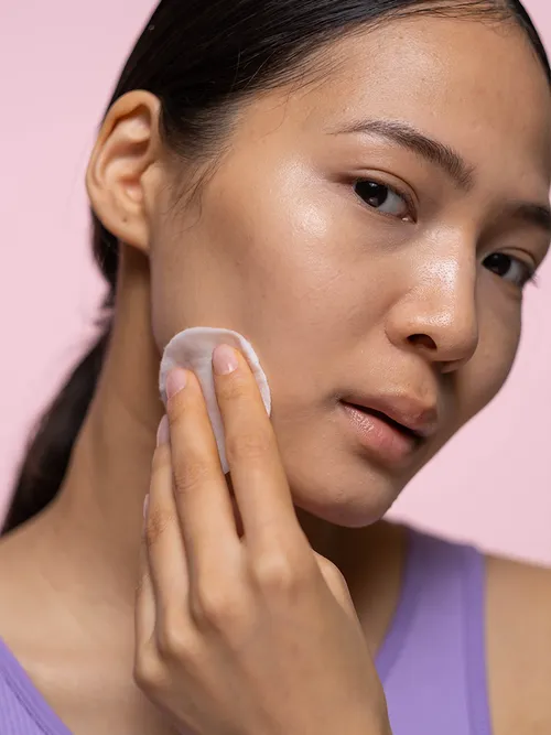 Frau mit lila Top wischt sich mit einem Wattepad über das Gesicht.