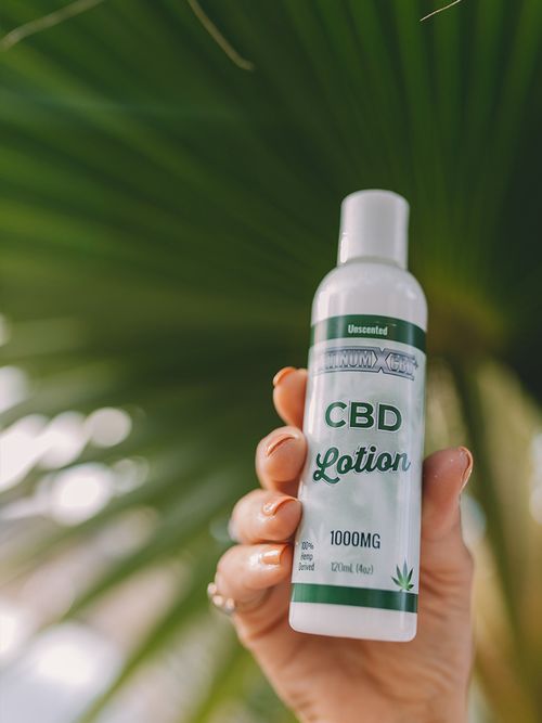 Hand die eine CBD Lotion in die Luft hält.