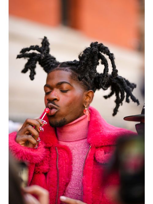 Lil Nas X wears red pendant earrings, a pink glitter wool turtleneck pullover, a red fluffy oversized long coat, outside Coach, during New York Fashion Week, on February 13, 2023 in New York City.