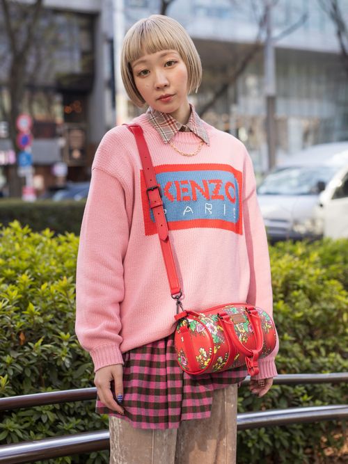 A TFW guest wears a pink checkered flannel shirt, a gold chain, a pink KENZO jumper, a red flower print mini duffle bag, and dusty pink velvet trousers.