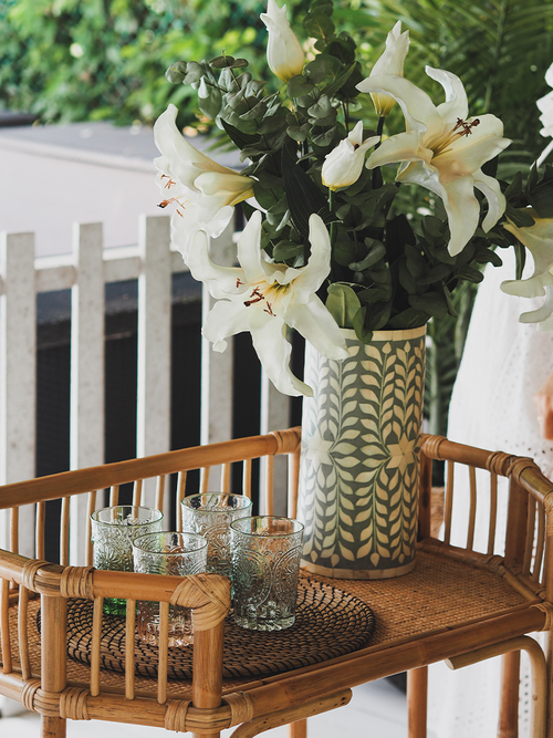 Eine Hausbar aus Bambus, mit einer Vase Lilien und einigen Gläsern darauf.