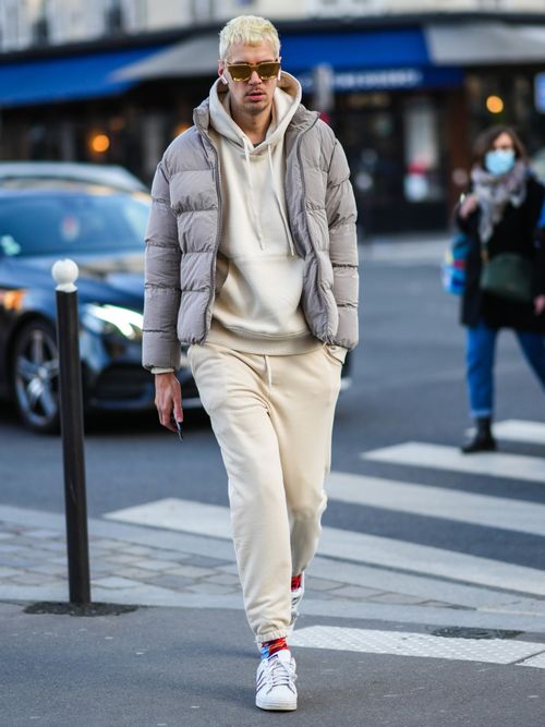 Street Style Look von der Paris Fashion Week, wo ein Mann einen weißen Hoodie, beige Sweatpants mit grauer Daunenjacke trägt.