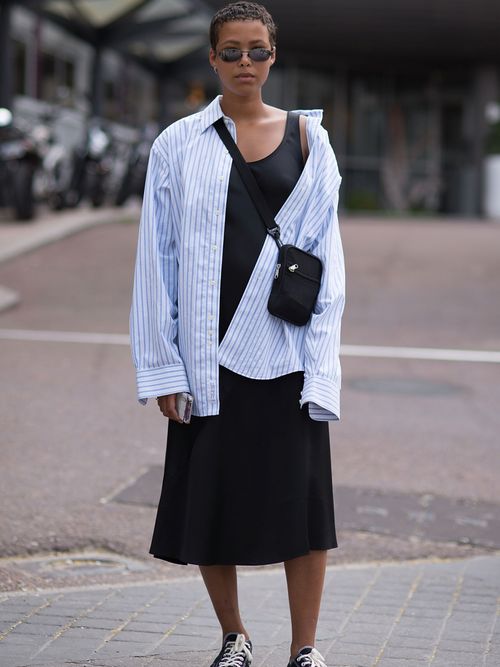 Street Style Look von der Paris Fashion Week. Ein Gast trägt ein schwarzes Kleid mit gestreifter Bluse, Umhängetasche und Converse.