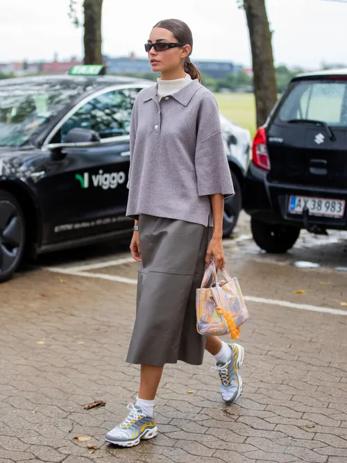 Street Style Look von der Copenhagen Fashion Week. Ein Gast trägt ein kurzärmeliges Poloshirt mit Rollkragen darunter, einen Lederrock und sportliche Sneakers.