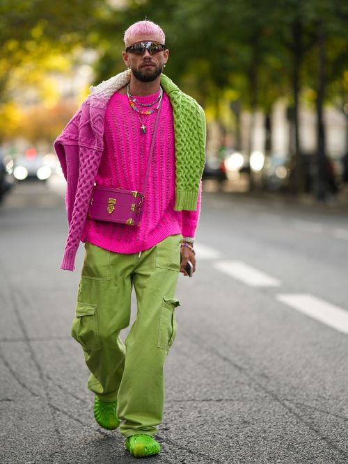 Influencer Karb trägt ein pinkes Oberteil mit Colorblocking Pullover über die Schultern und dazu eine grüne Hose auf der Paris Fashion Week.