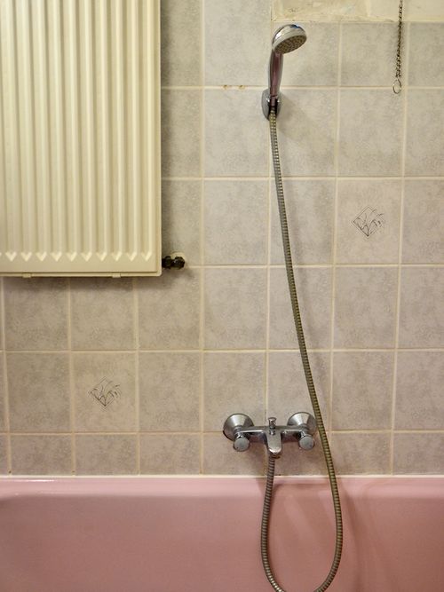 Rosa Badewanne vor einer grau gefließten Wand.