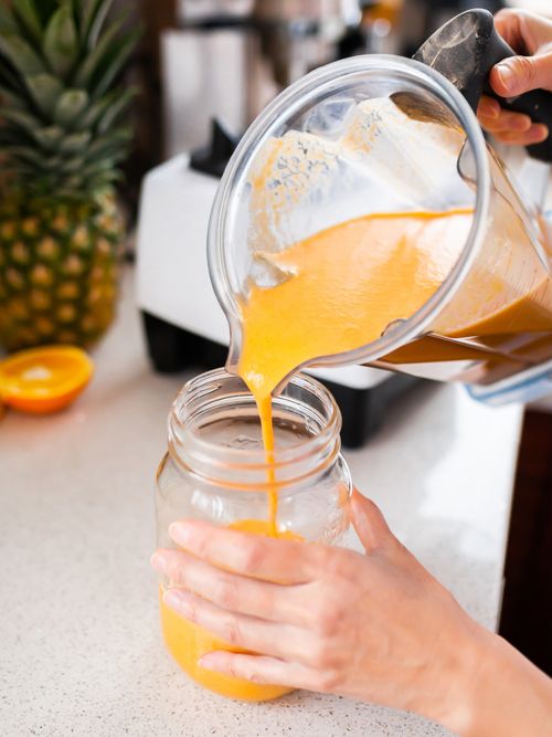 Ein orangener Smoothie wird vom Smoothiermixer in ein Glas gefüllt.