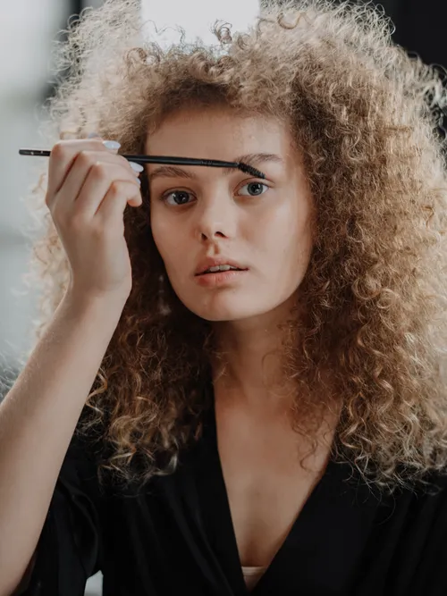 Frau mit lockigem Haar die sich gerade ihre Augenbrauen bürstet