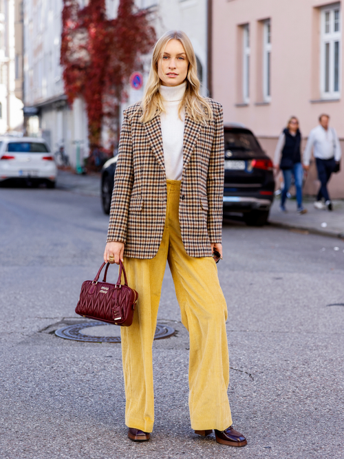 Model und Influencer Marlies-Pia Pfeiffhofer trägt eine Cordhose in Senfgelb mit einem Karoblazer und weißem Rollkragenpullover, dazu eine bordeauxrote Clutch in München