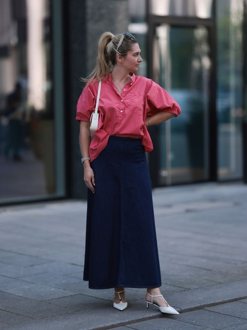 Josephine Kröger trägt eine pinke Bluse mit dunkelblauen Midirock und weißer Tasche mit spitzen Kitten Heels in Düsseldorf.