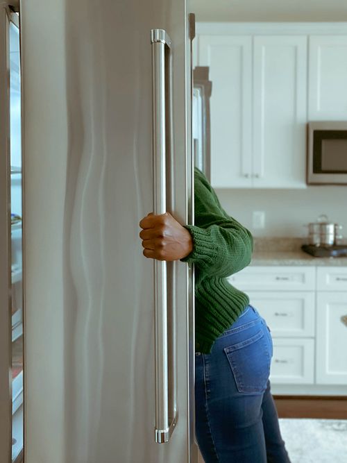 Frau mit grünem Pulli schaut in großen Kühlschrank