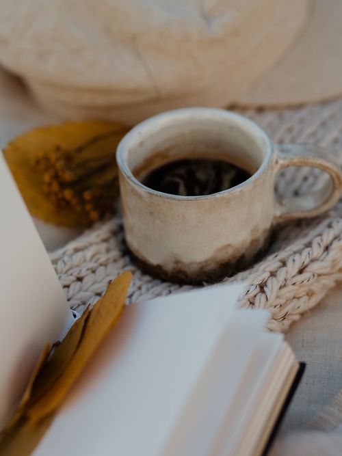 Buch und eine Steinguttasse stehen auf einer gestrickten Decke.