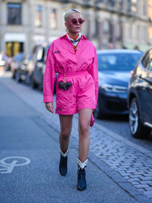 Ein Street Style Look von der Copenhagen Fashion Week, wo ein Gast ein pinkes Ensemble trägt, mit Cowboyboots und Sonnenbrille.