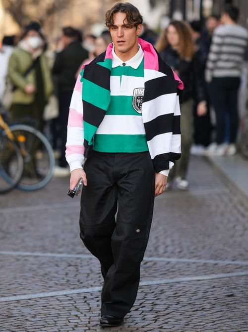Street Style Look, auf der Milan Fashion week. Wo ein Mann ein gestreiftes Rugby-Shirt mit einem gestreiften Pullover über die Schultern, mit einer schwarzen Hose trägt.