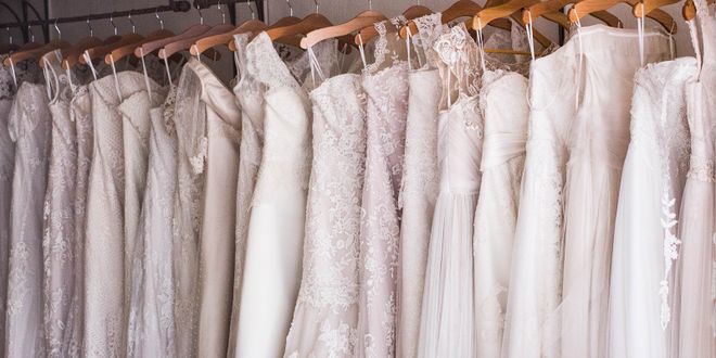 Weiße Brautkleider die nacheinander auf braunen Kleiderbügeln hängen.