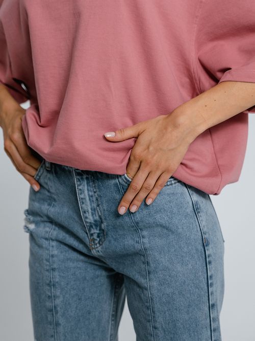 Close up von einer Frau mit einer hellen Jeans und einem pinken Pulli.