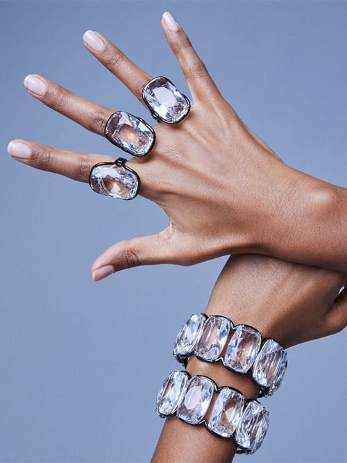 Eine Hand mit 3 großen Kristallringen und ein Handgelenk mit zwei großen Kristallarmbändern.