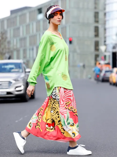 Model Zoe Helali trägt einen grünen gemusterten Pullover mit einem rot-gemusterten Rock und Sneaker in Berlin