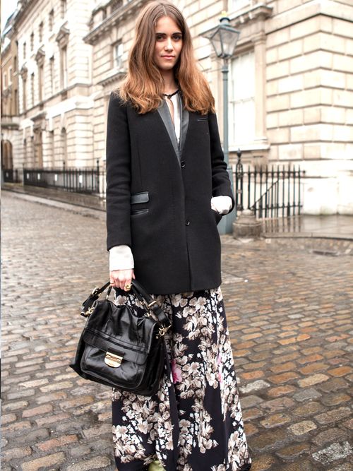 A street style photograph taken at fashion week, featuring a women wearing a floral skirt and black blazer.