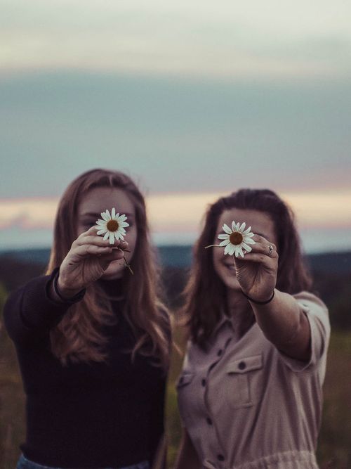 Zwei Frauen halten Margaritten in ihren Händen und in die Linse der Kamera