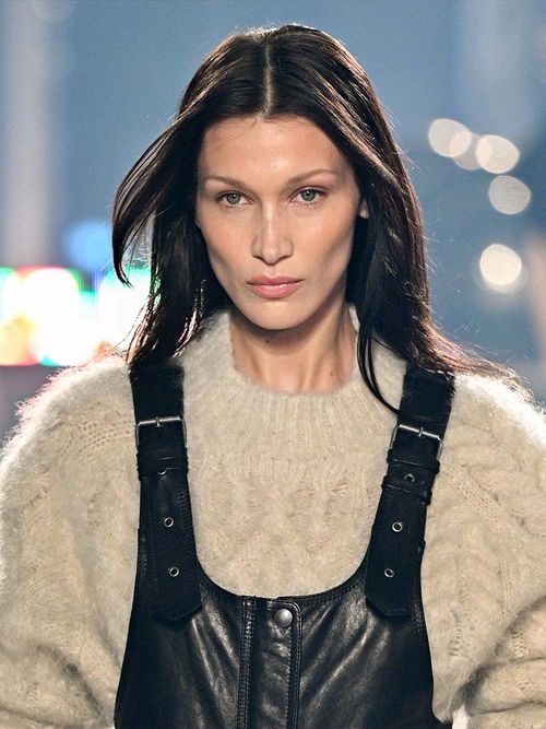 Bella Hadid auf mit einem weißen Strickpullover und einer Lederlatzhose.