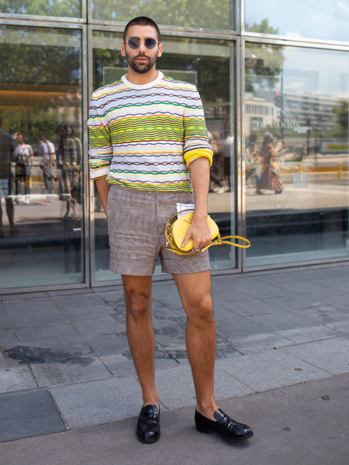 Street Style Look von der Paris Fashion Week, wo ein Gast einen gestreiften Strickpulli mit gestreifter kurzen Hose und gelber Tasche trägt.