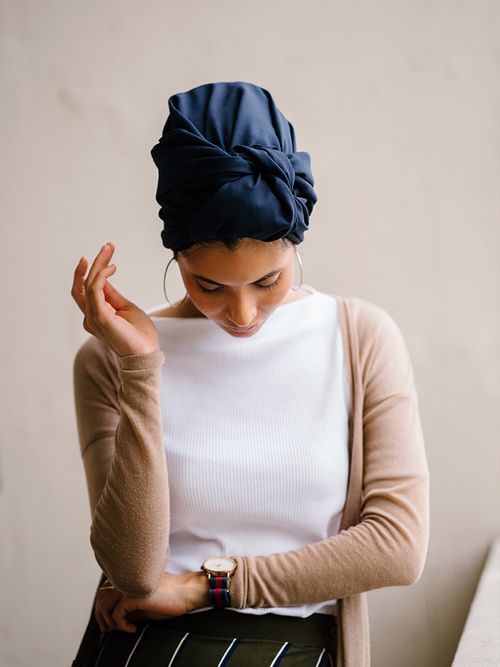 Frau mit weißem Shirt und beigen Cardigan trägt einen dunkelblauen Turban.