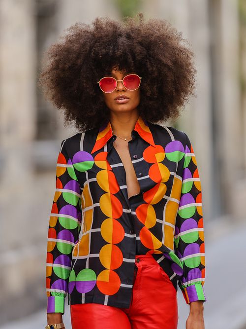 Streetstyle mit einer bunt gemusterten Bluse zu einer roten Hose und einer Sonnenbrille mit roten Gläsern.