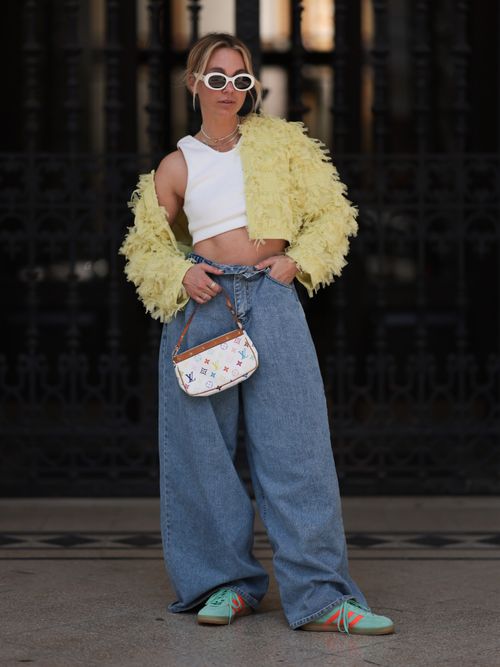 Karin Teigl trägt eine Cropped-Jacke mit weißem Crop-Top, Baggy Jeans, Louis V Tasche und Adidas Original Sneaker in Wien.