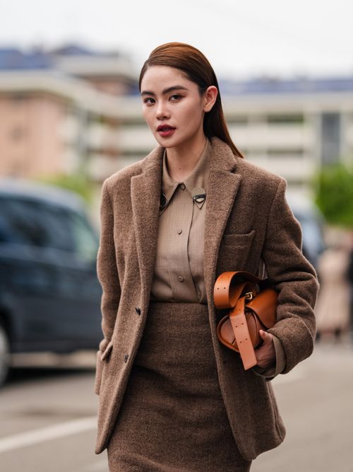 Doudou Babe trägt ein braunes Woll-Ensemble mit brauner Bluse und orangefarbener Tasche auf der Milan Fashion Week.