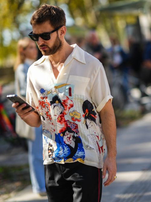 Street Style Look von der Paris Fashion Week wo ein Gast ein buntes Kurzarm-Hemd mit Reverskragen trägt und einer schwarzen Hose.