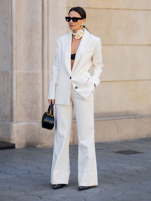 Zina Charkoplia trägt einen weißen Hosenanzug mit schwarzem Bh, schwarzer Tasche und Blumen-Choker um den Hals in Barcelona.