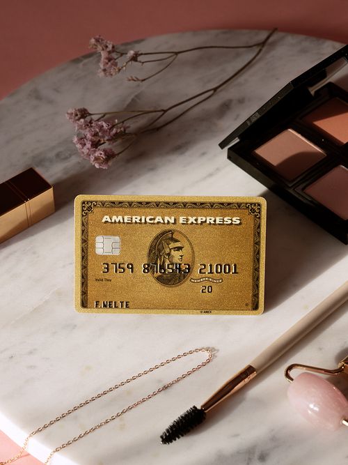 Ein rundes Marmortablett auf dem neben Schminkutensilien auch noch eine goldene Amex Kreditkarte liegt.
